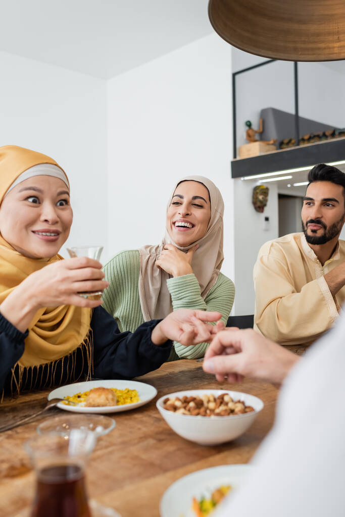 幸せなイスラム教徒の家族の近くでお茶を飲んでいる興奮したアジアの女性 - 写真・画像