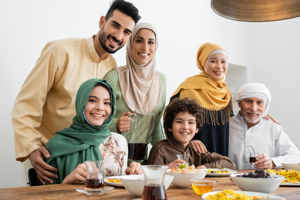 Famille musulmane multiculturelle souriant à la caméra près du pilaf servi et du thé - Photo, image
