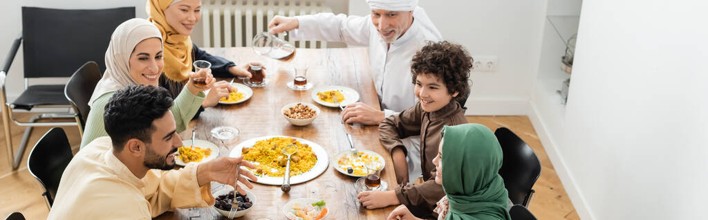 άποψη υψηλής γωνίας του ευτυχισμένη πολυεθνική μουσουλμανική οικογένεια έχοντας δείπνο στο σπίτι, πανό - Φωτογραφία, εικόνα