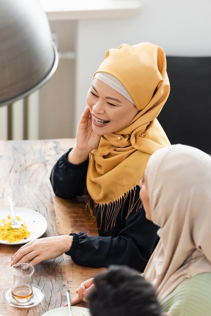 hoge hoek uitzicht van moslim aziatische vrouw glimlachen in de buurt van Arabische dochter tijdens het diner - Foto, afbeelding