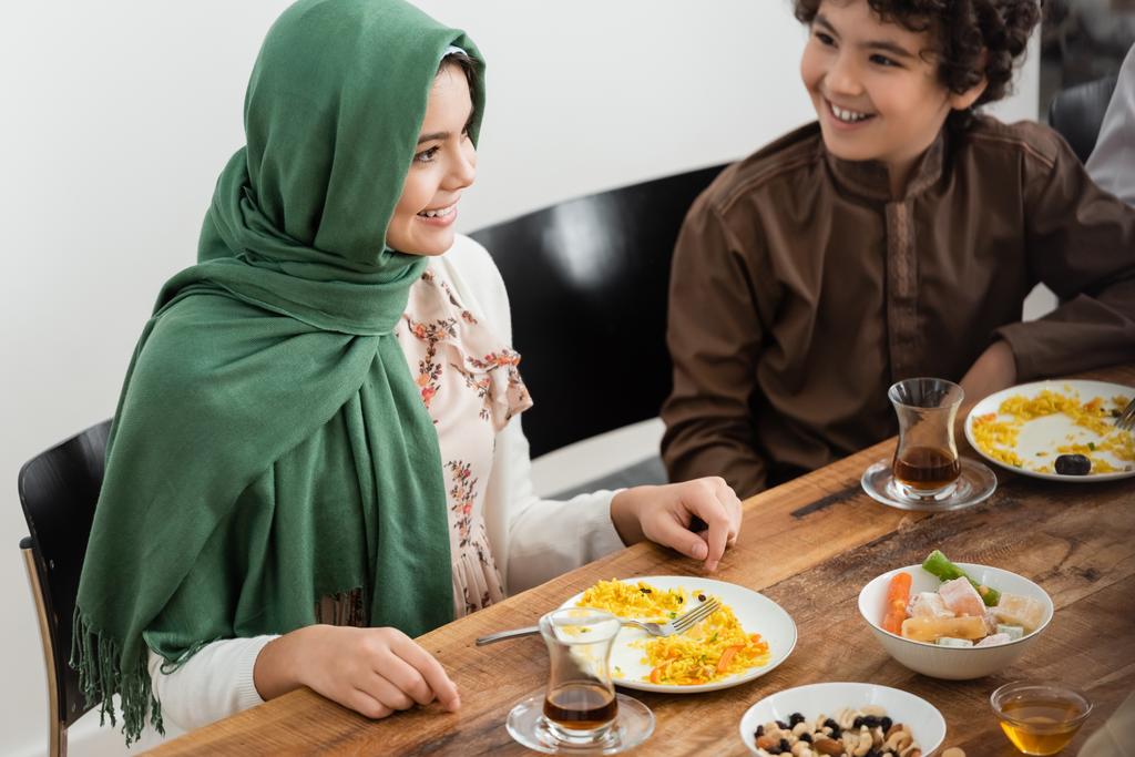 Μουσουλμάνα κοπέλα χαμογελά κοντά στον αδερφό της Αραβίας κατά τη διάρκεια του οικογενειακού δείπνου - Φωτογραφία, εικόνα