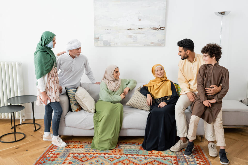 Evdeki Müslüman ailenin yanındaki koltukta oturan mutlu ırklar arası kadınlar. - Fotoğraf, Görsel