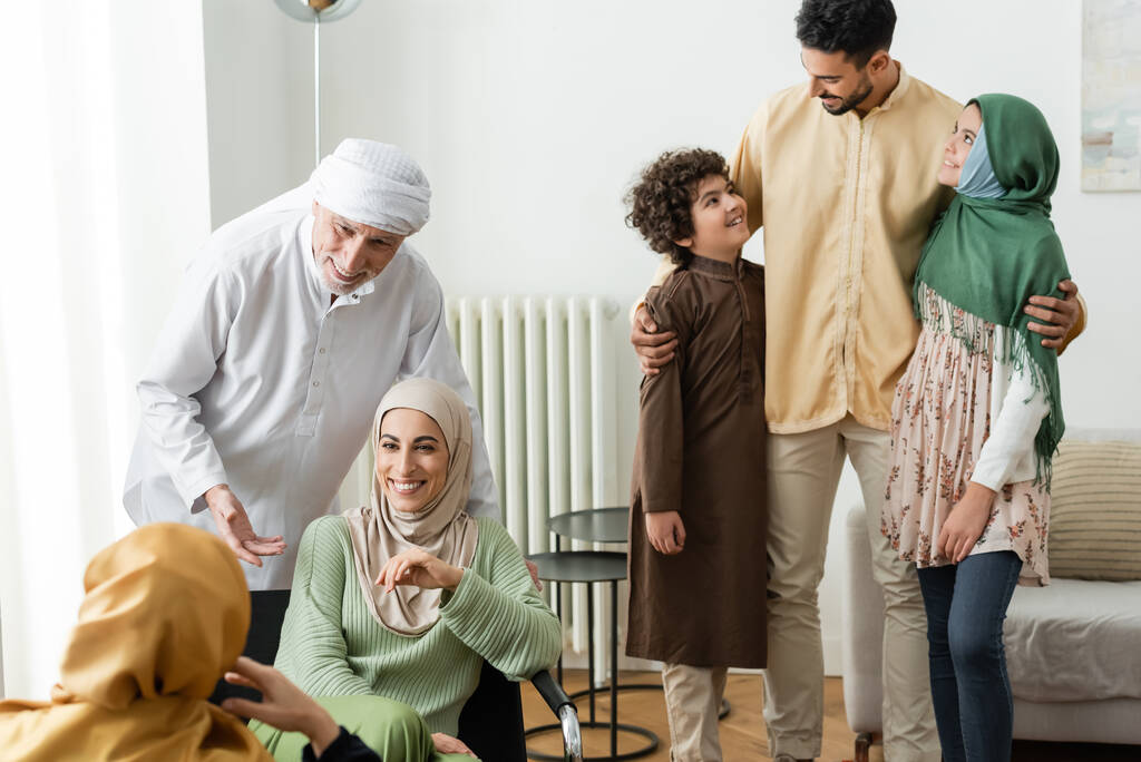 árabe hombre abrazando interracial niños cerca musulmán familia en casa - Foto, imagen