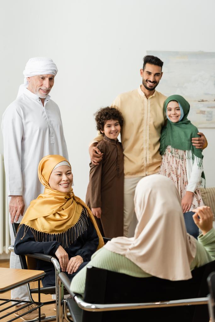 χαμογελαστός αραβικός άνδρας αγκαλιάζει τα παιδιά κοντά στην πολυεθνική μουσουλμανική οικογένεια μιλώντας στο σπίτι - Φωτογραφία, εικόνα