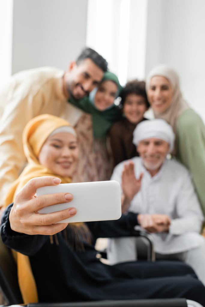 happy asian woman taking selfie with blurred interracial muslim family - Photo, Image