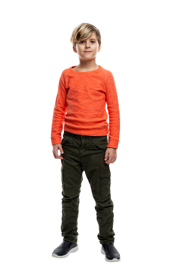 少年は立っている。ダークジーンズの男とオレンジのセーター。白い背景に隔離されている。垂直. - 写真・画像