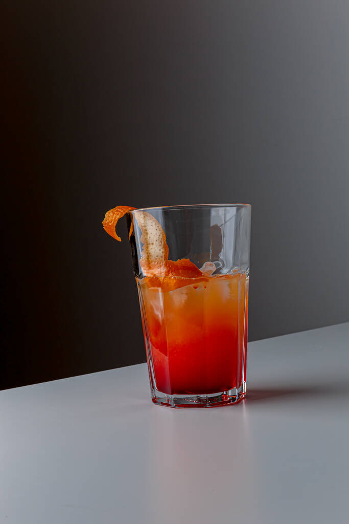Fruchtgesunder Cocktail aus Mangosaft, Orangenschalen-Spirale und Eis auf dunkelschwarzem Hintergrund. - Foto, Bild
