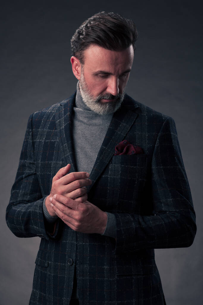 Portret van een stijlvolle elegante senior zakenman met een baard en casual zakelijke kleding in fotostudio geïsoleerd op donkere achtergrond gebaren met handen. Hoge kwaliteit foto - Foto, afbeelding
