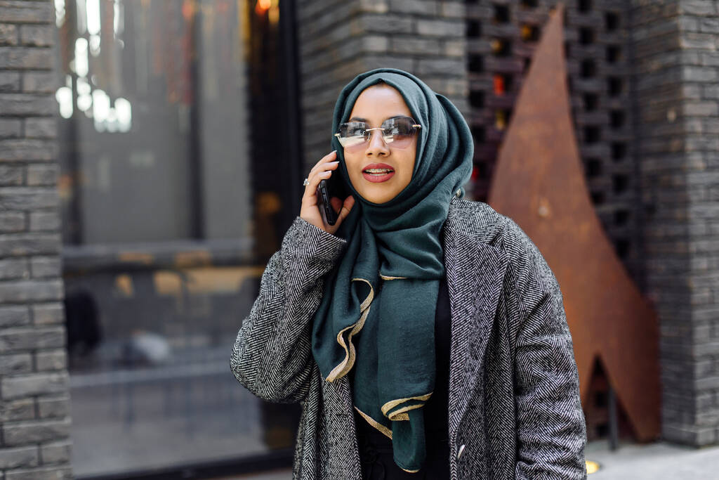 Портрет мусульманской девушки в зеленом хиджабе и солнечных очках на улице - Фото, изображение
