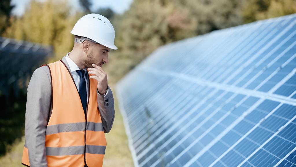 pensive businessman in safety vest and hardhat looking at solar panels - Φωτογραφία, εικόνα