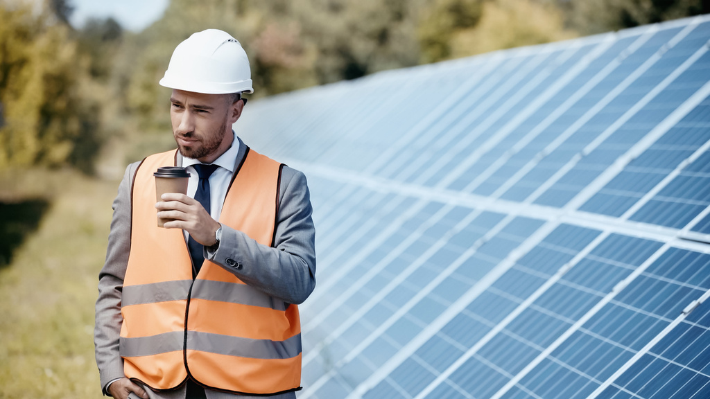 businessman in hardhat holding coffee to go near solar batteries outside - Photo, Image