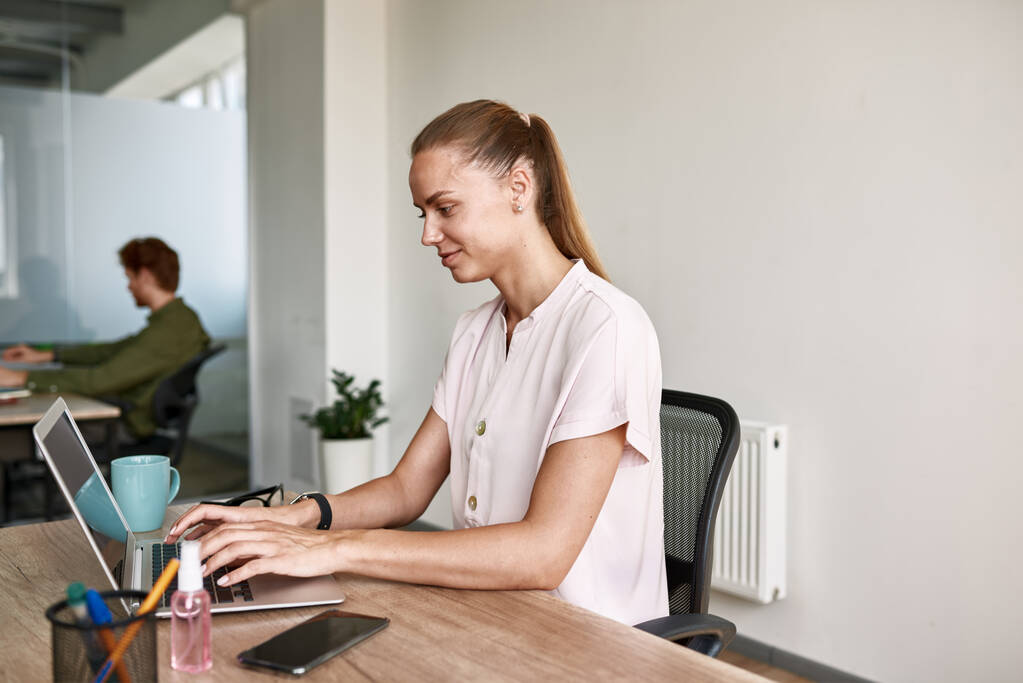 Smiling girl typing on laptop while working - Photo, image