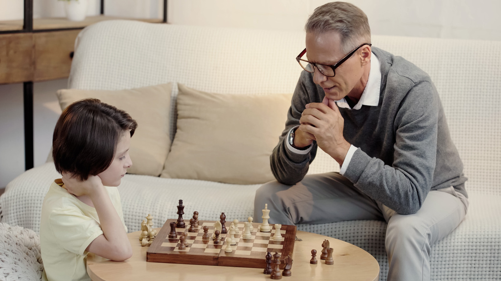 avô pensativo em óculos e neto inteligente jogando xadrez na sala de estar - Foto, Imagem