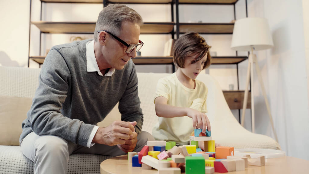 middle aged grandfather in glasses playing building blocks with boy - Fotoğraf, Görsel
