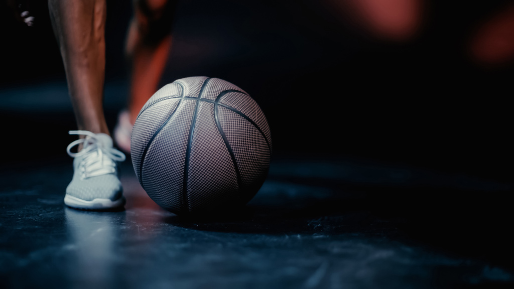 Ausgeschnittene Ansicht eines Sportlers, der in der Nähe von Basketball auf dunklem Hintergrund steht - Foto, Bild