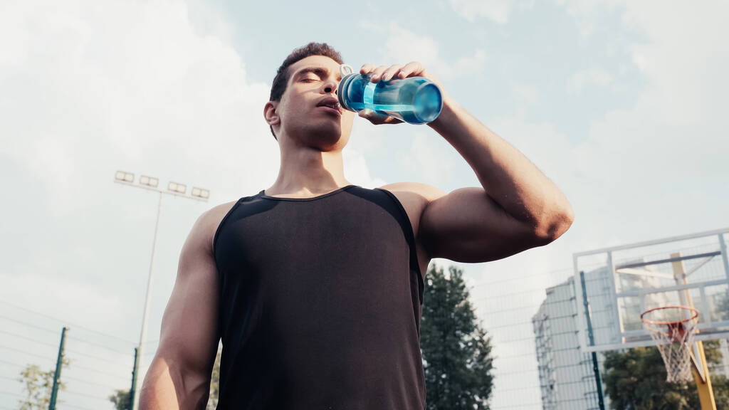 スポーツボトルの水を屋外で飲む二人種スポーツマンの低角度ビュー - 写真・画像