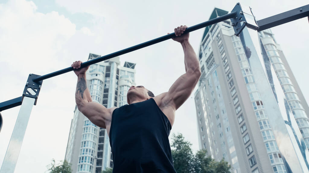 low angle view of tattooed mixed race man exercising on horizontal bar outdoors - Photo, Image