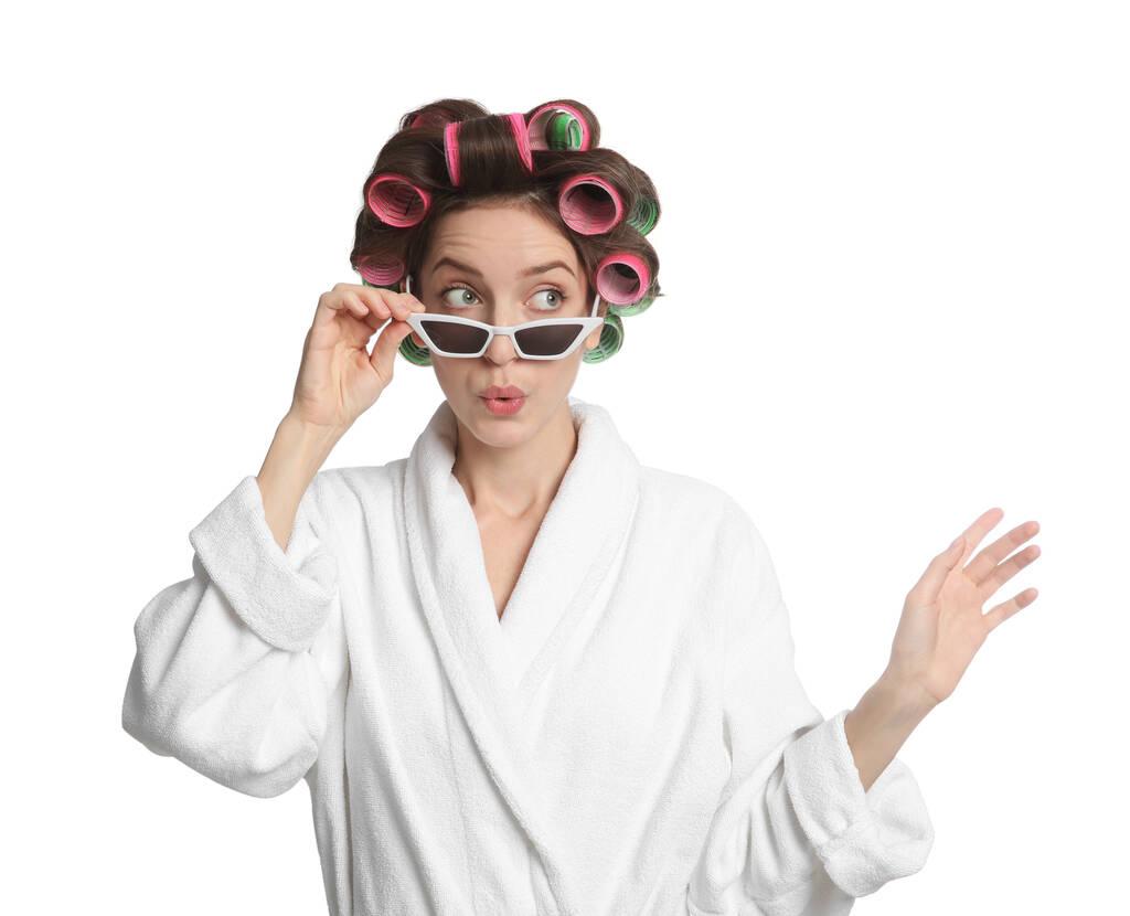 Emotional young woman in bathrobe with hair curlers and sunglasses on white background - Photo, Image
