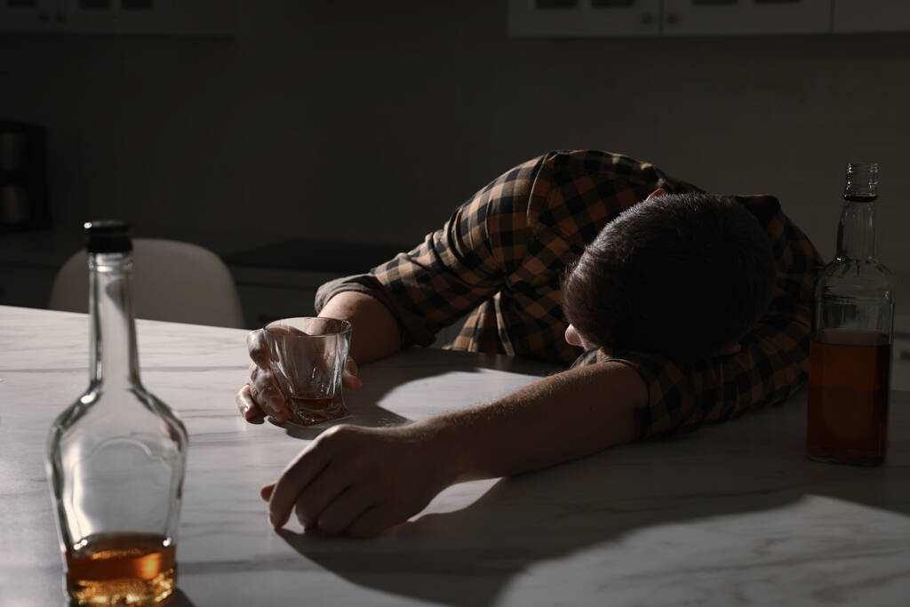 Залежний чоловік з алкогольним напоєм спить за столом на кухні
 - Фото, зображення