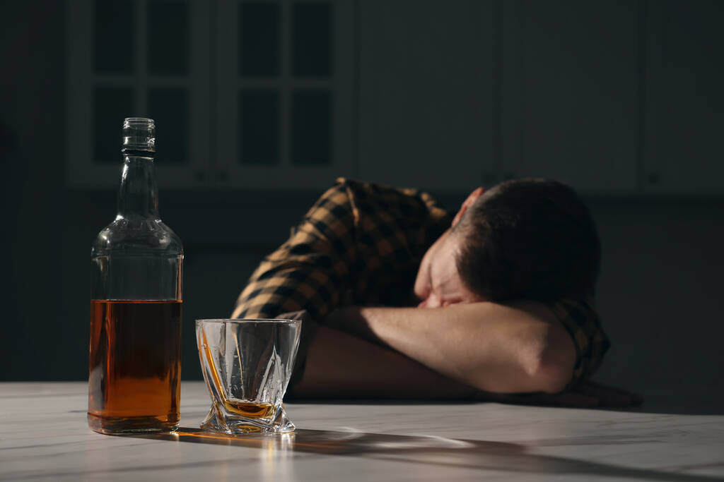 Addicted man sleeping at table in kitchen, focus on alcoholic drink. Space for text - Photo, Image