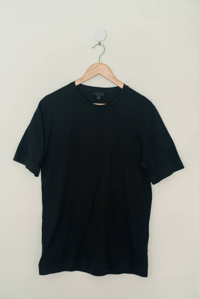 black t-shirt hanging with wood hanger on wall - Fotó, kép