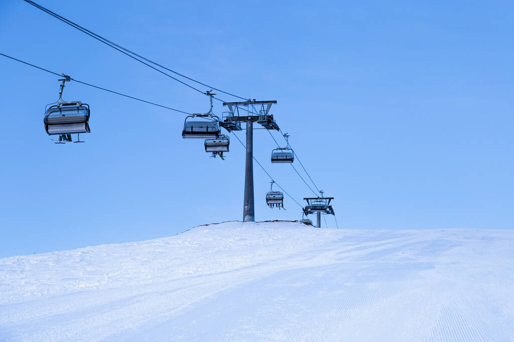 Лыжный подъемник на вершине горы, лыжный склон, подготовленный для катания на лыжах, синяя монохромная зима минимального стиля в горнолыжном курорте Шерегеш. Белый снег, чистое небо, кабельная дорога и маленькие люди на пике - Фото, изображение