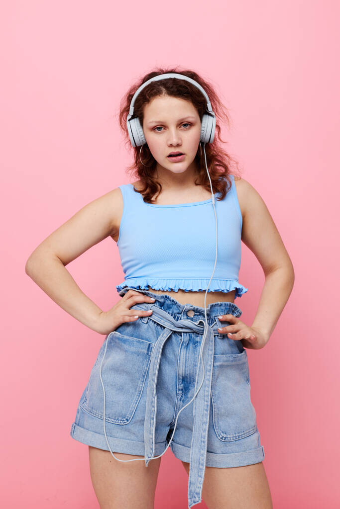 portrét mladé dívky ve sluchátkách poslech hudby na růžovém pozadí beze změny - Fotografie, Obrázek