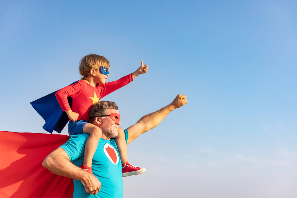Superheld Senior Mann und Kind spielen im Freien. Superhelden-Opa und -Junge amüsieren sich gemeinsam vor blauem Himmel. Familienurlaubskonzept. Glücklicher Vatertag - Foto, Bild