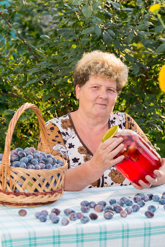 oudere vrouw met een pot van plum compote - Foto, afbeelding