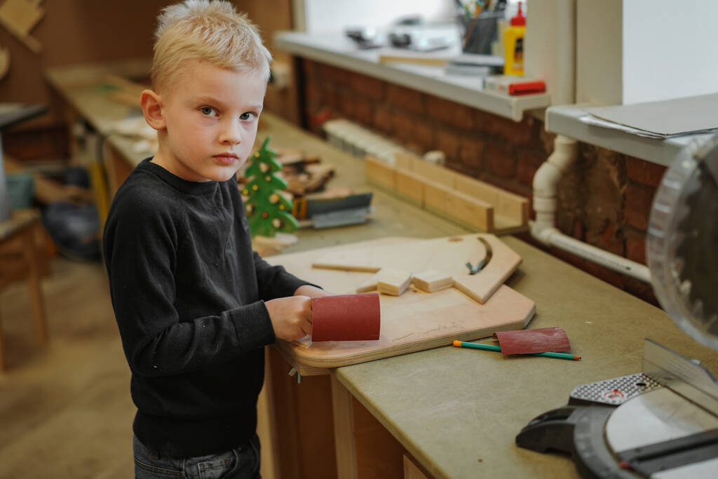 cute caucasian preschooler boy msking a wooden christmas tree in joinery class. Image with selective focus - Photo, Image