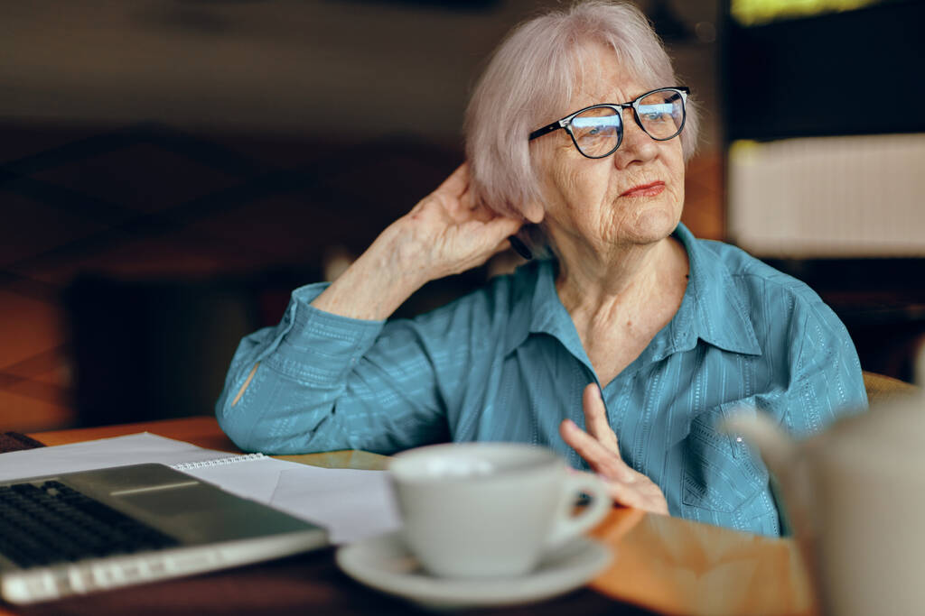 Szczęśliwa starsza kobieta w okularach siedzi przy stole przed laptopem Styl życia niezmieniony - Zdjęcie, obraz