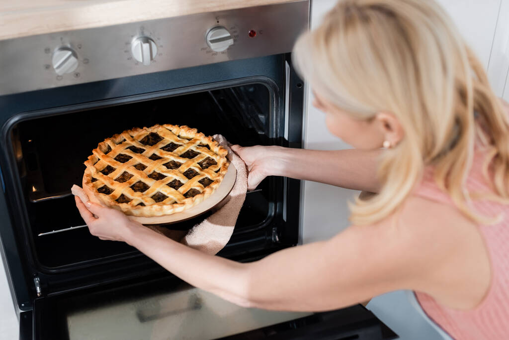 Домашний пирог в руках размытой женщины и духовка на кухне  - Фото, изображение