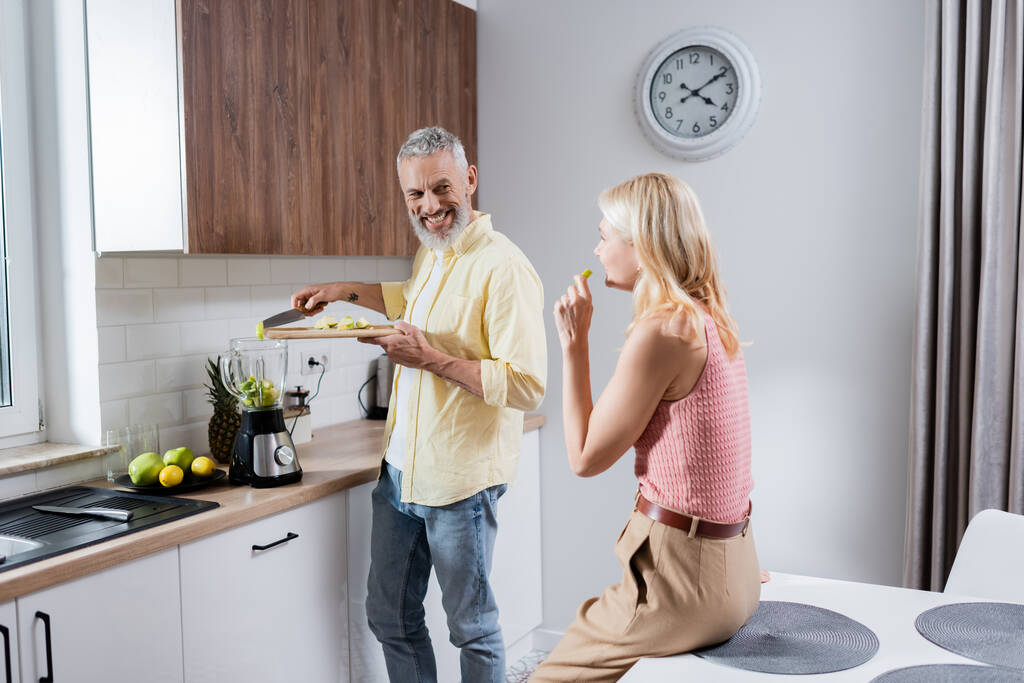 Pozitív férfi hozzá gyümölcs turmixgép közelében feleség a konyhában  - Fotó, kép
