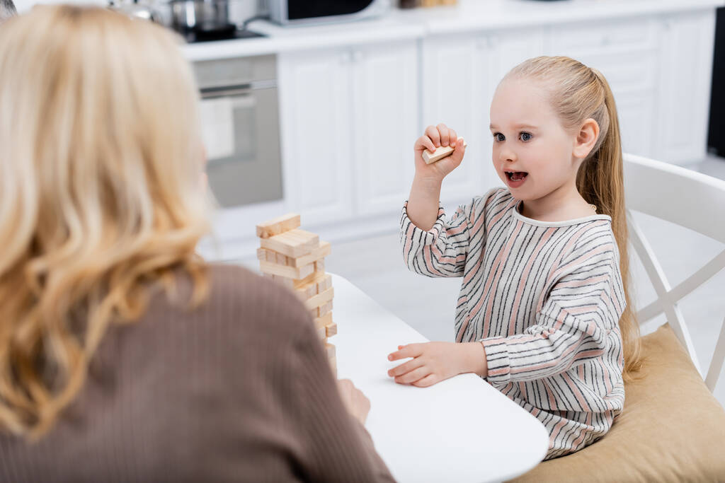 menina espantada jogando blocos de madeira jogo perto de avó borrada na cozinha - Foto, Imagem