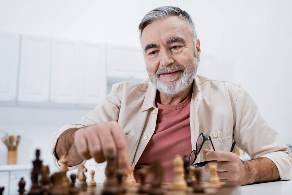 sonriente hombre mayor jugando ajedrez en la cocina en casa - Foto, imagen
