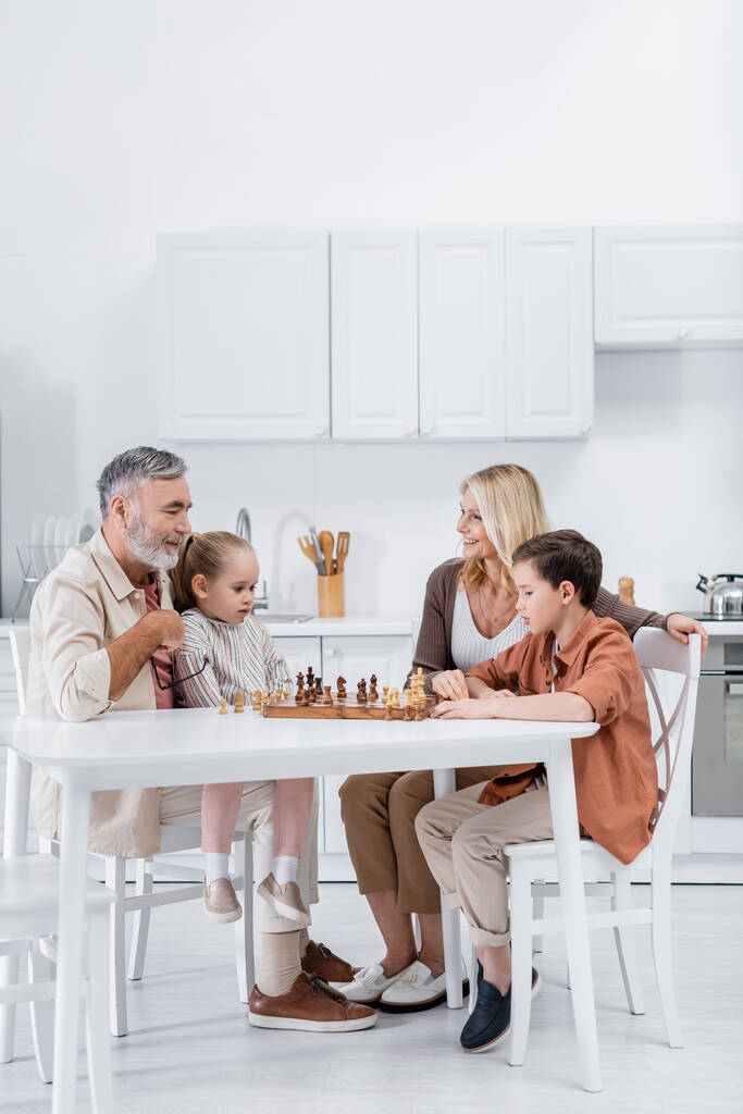 ευτυχισμένο ζευγάρι που παίζει σκάκι με εγγόνια στην κουζίνα - Φωτογραφία, εικόνα