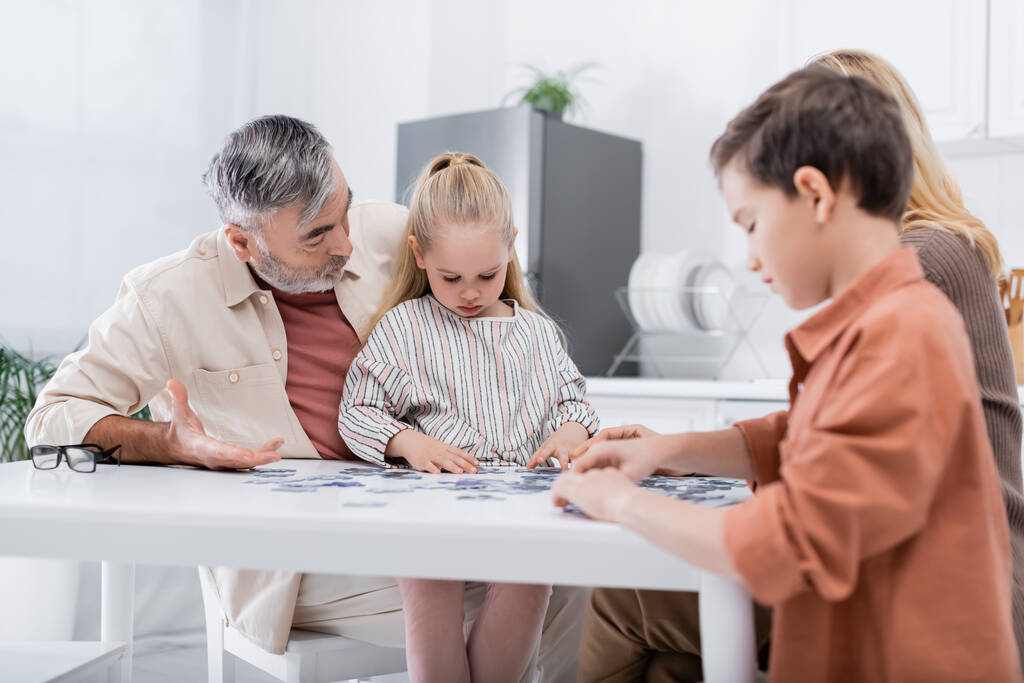 kids playing jigsaw puzzle game with grandparents in kitchen - Photo, Image