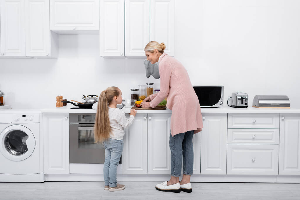 uśmiechnięta dojrzała kobieta z małą wnuczką gotującą razem w nowoczesnej kuchni - Zdjęcie, obraz