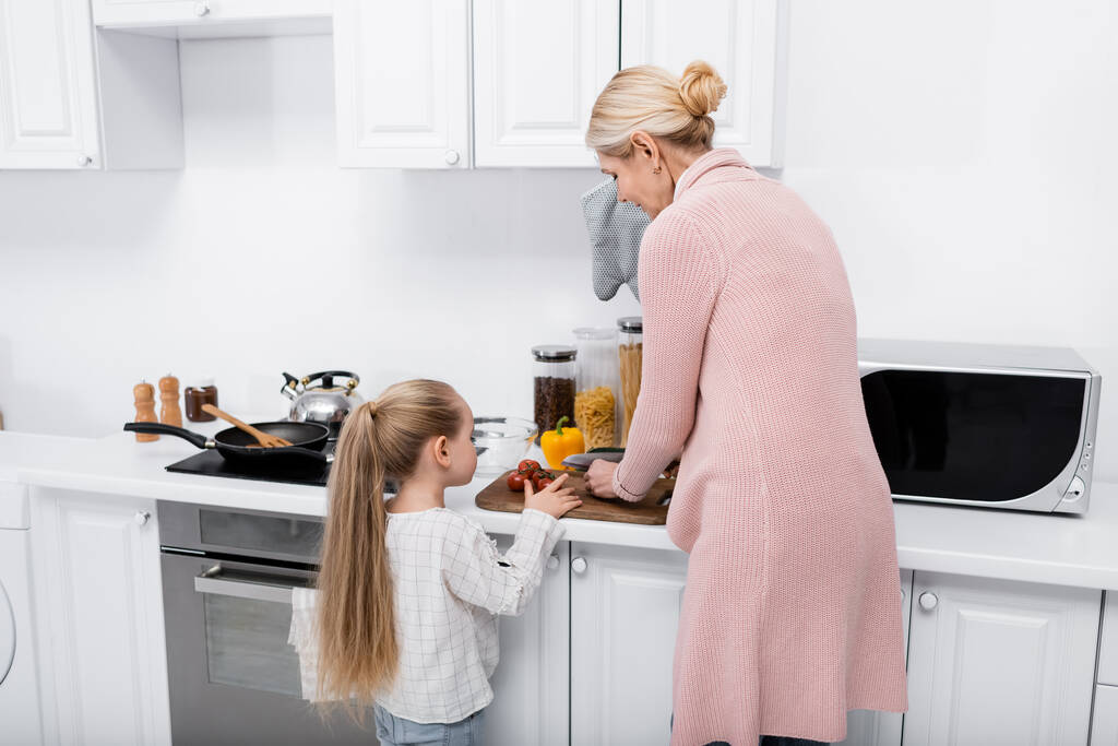 middle aged woman cutting vegetables near granddaughter in kitchen - Photo, Image