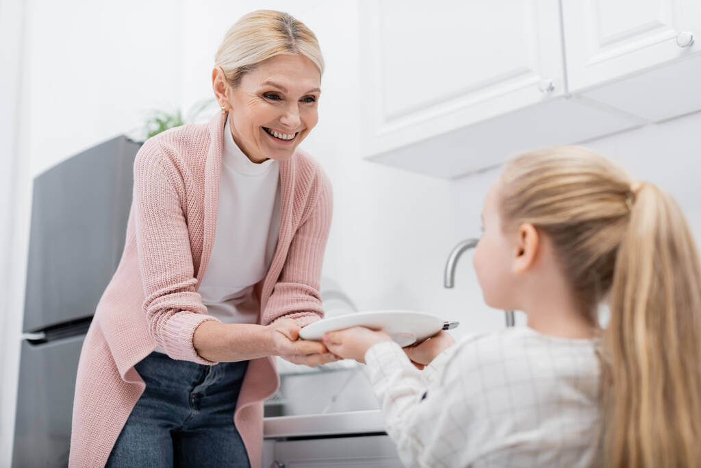 menina borrada segurando placa enquanto ajuda a vovó feliz na cozinha - Foto, Imagem