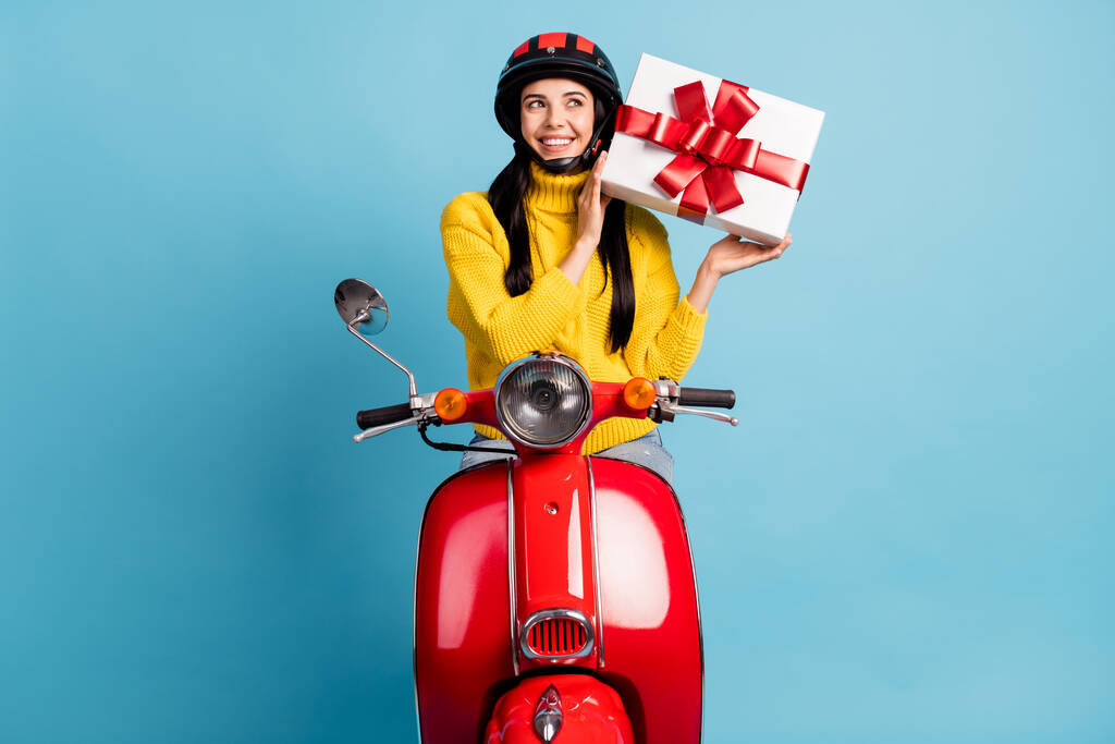 Фотопортрет молодой женщины на ретро-мотоцикле, пытающейся угадать, что внутри настоящей коробки выделено ярко-голубым цветом фона. - Фото, изображение