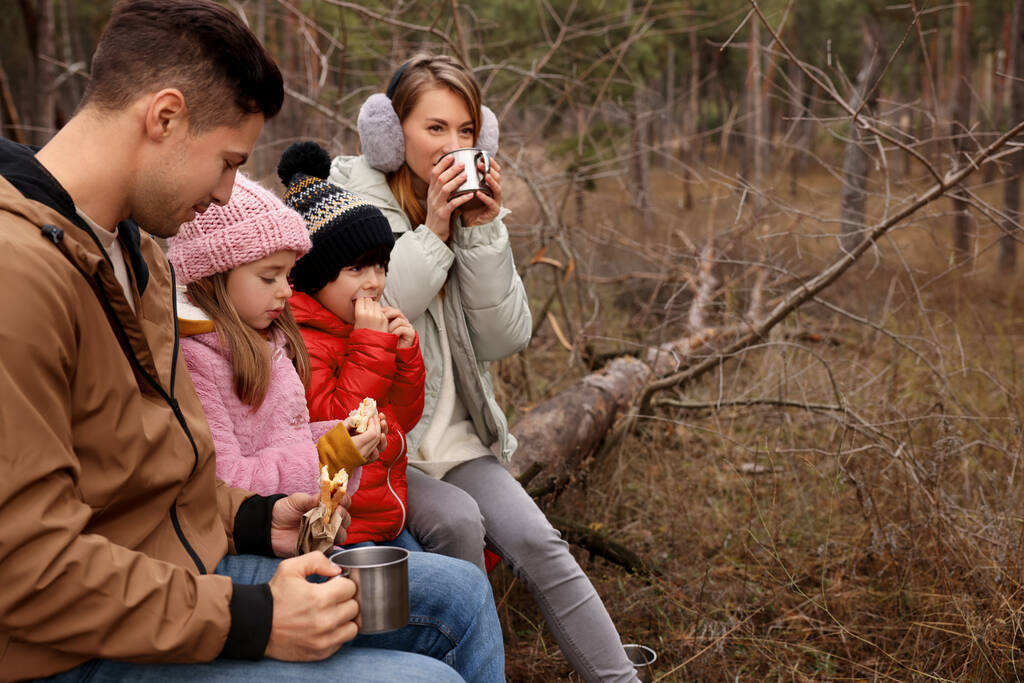 Happy family with sandwiches and hot drinks spending time together in forest - Photo, Image