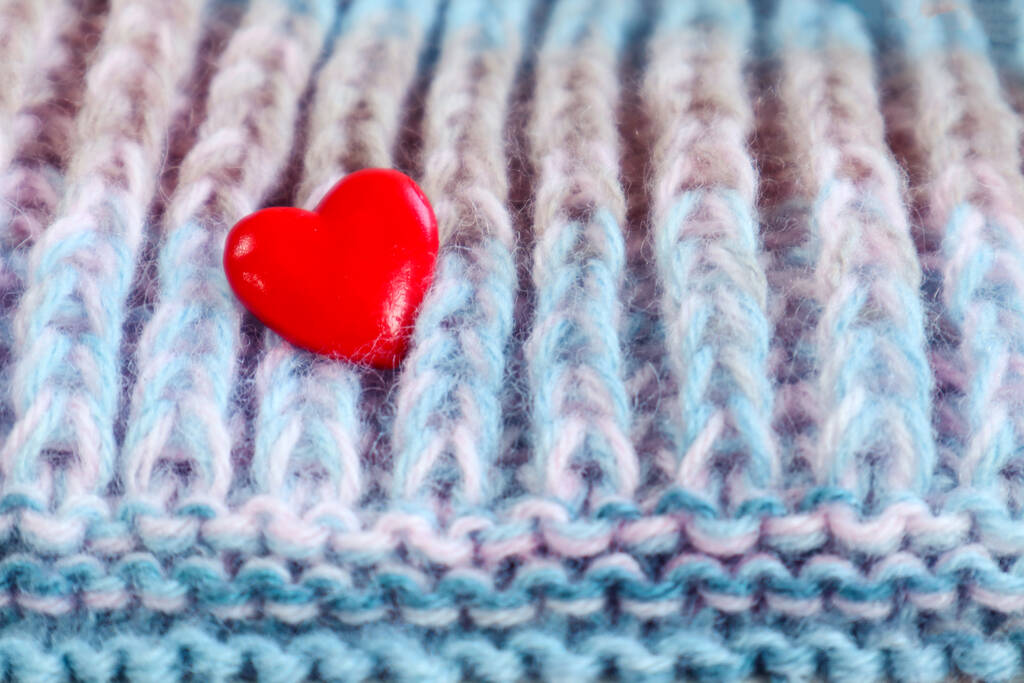 Κάνουμε το αγαπημένο μας κέντημα: μια κόκκινη καρδιά σε ένα πλεκτό ύφασμα, κοντινό πλάνο - Φωτογραφία, εικόνα