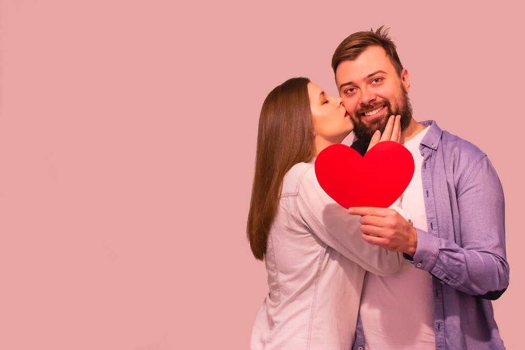 Lovely couple with heart shape against pink background woman kissing a man isolated  - Photo, Image