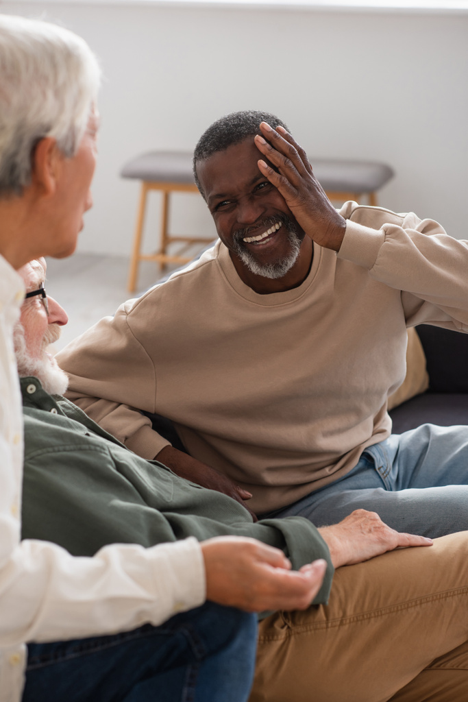 Positiver afrikanisch-amerikanischer Mann sieht multiethnische Freunde im Gespräch zu Hause an  - Foto, Bild