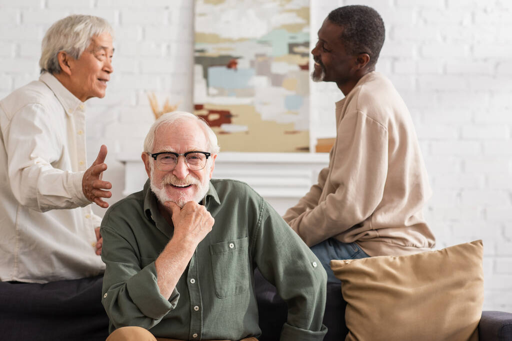 vieil homme positif regardant la caméra près des amis interraciaux à la maison  - Photo, image