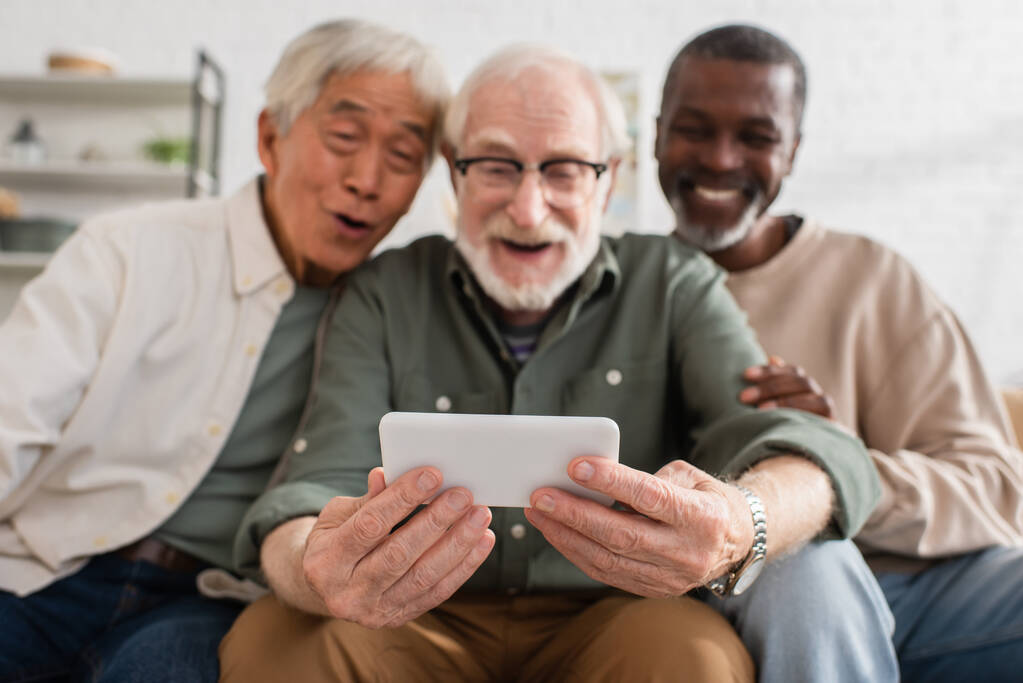Smartphone v rukou rozmazané starší muž v blízkosti mezirasových přátel doma  - Fotografie, Obrázek