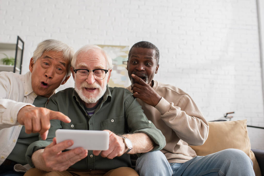 Шоковані міжрасові чоловіки дивляться на смартфон біля друга вдома
  - Фото, зображення