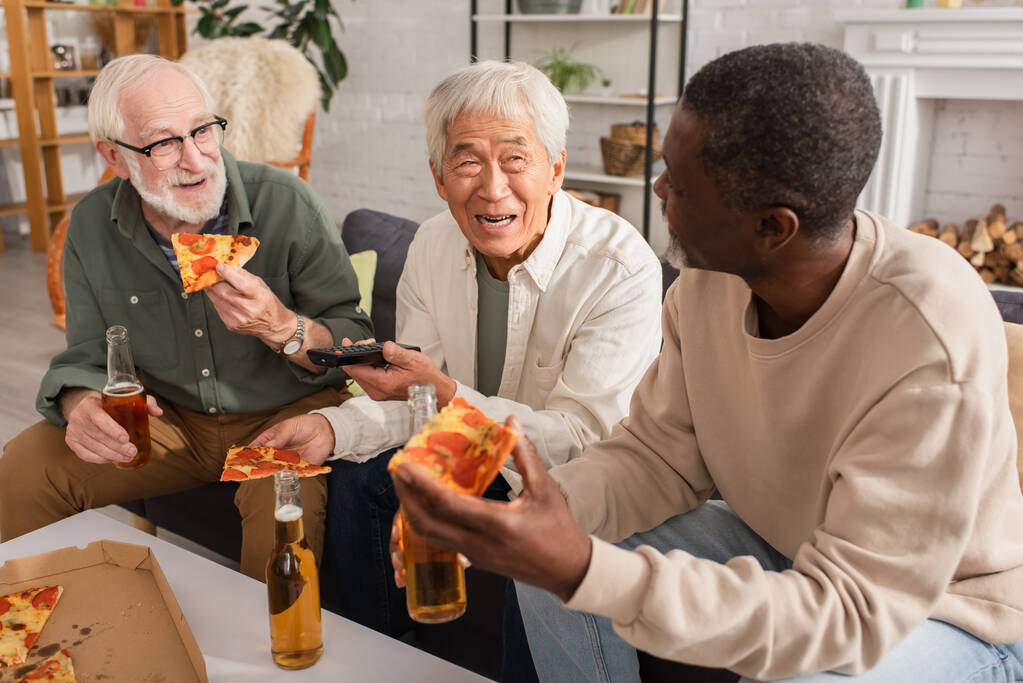Evde bira yanında pizza ve uzaktan kumanda tutan pozitif ırklar arası kıdemli adamlar var.  - Fotoğraf, Görsel