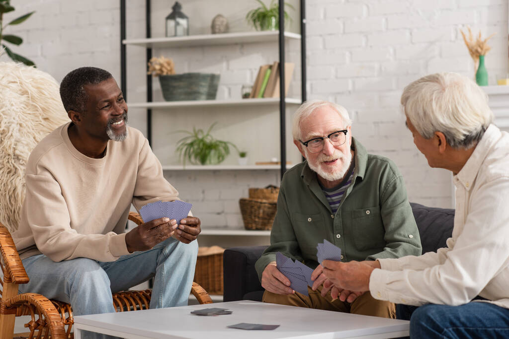 Ancianos interracial amigos hablando mientras jugando a las cartas en casa  - Foto, imagen